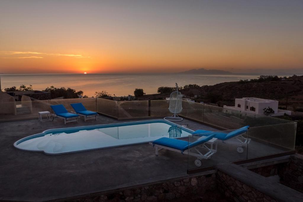 a pool with chairs and a sunset in the background at Queen of Santorini in Karterados