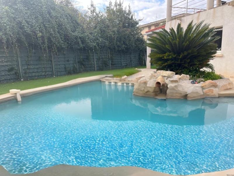 une grande piscine d'eau bleue avec des rochers dans une cour dans l'établissement Villa Marella, aux Lecques