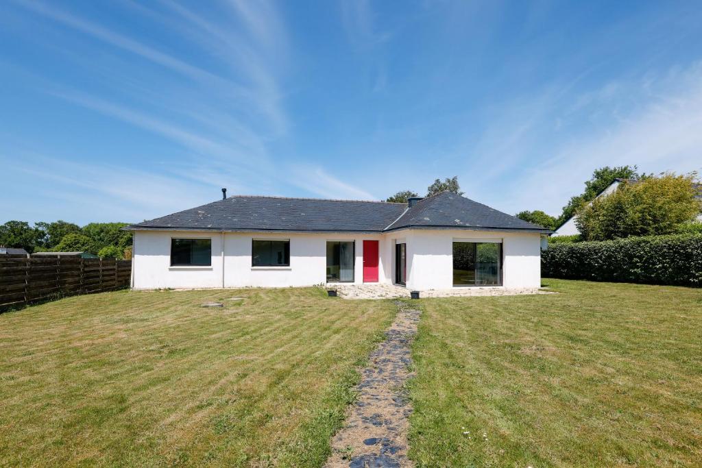 a white house with a red door on a yard at Grande maison familiale proche gr34 in Garlan