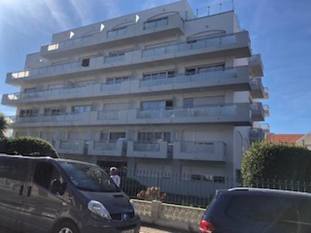 un grand bâtiment blanc avec des voitures garées devant lui dans l'établissement T2 RdC avec parking, plage à 50m, à Arcachon