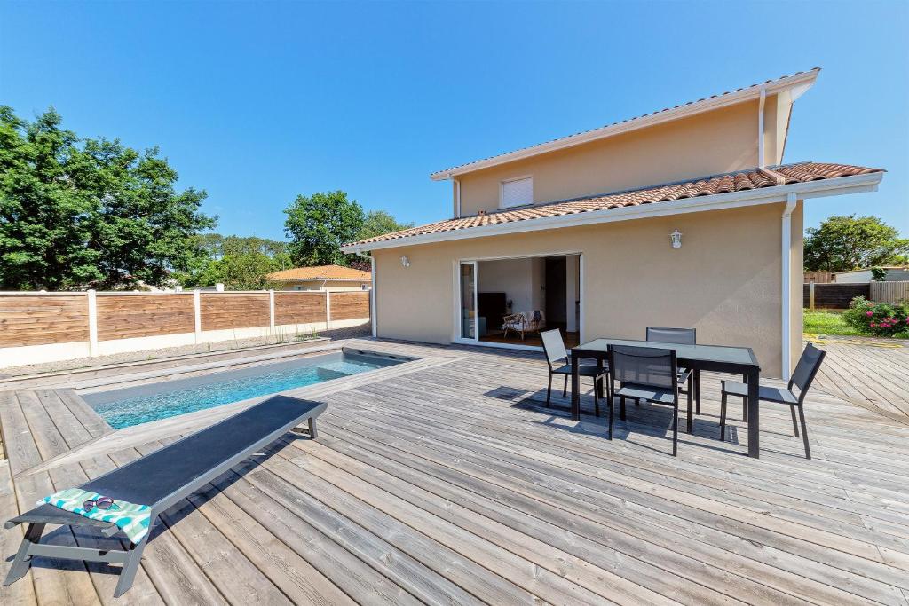 une terrasse en bois avec une table et des chaises à côté d'une maison dans l'établissement Villa Cazaline - Piscine Privée, à La Teste-de-Buch