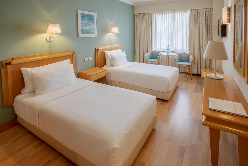 A bright twin room with two separate beds and a small seating area by the window.