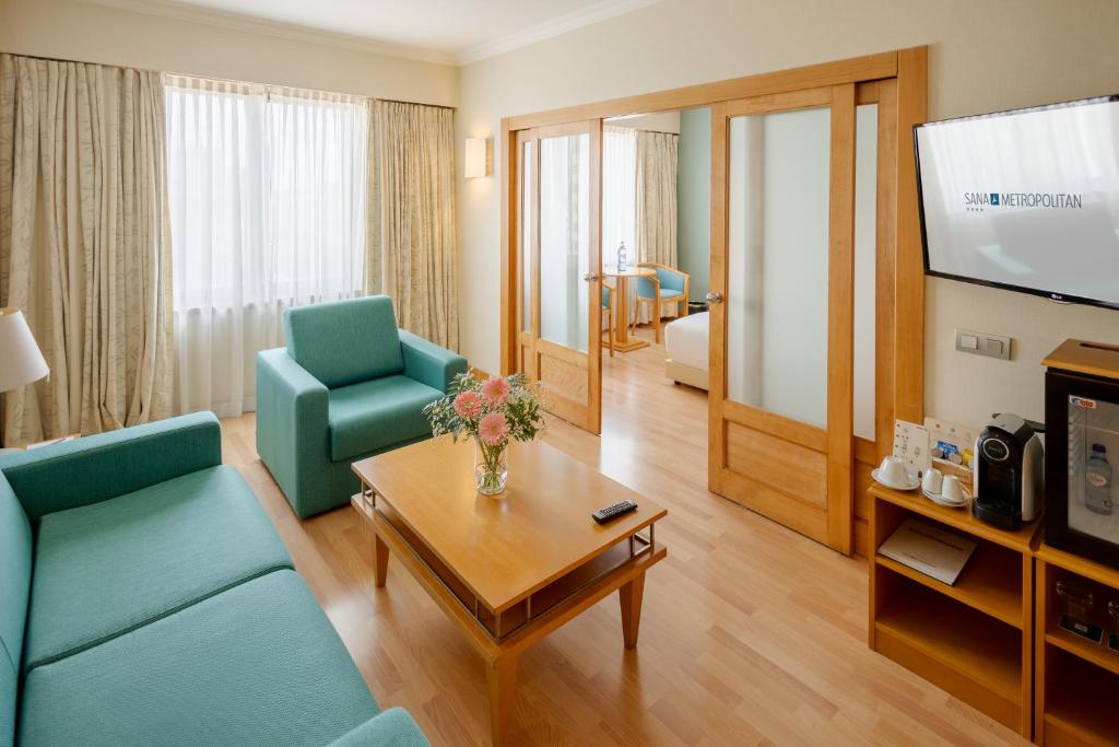 A separate sitting room pairs teal seating with a television and in-room refreshment station.