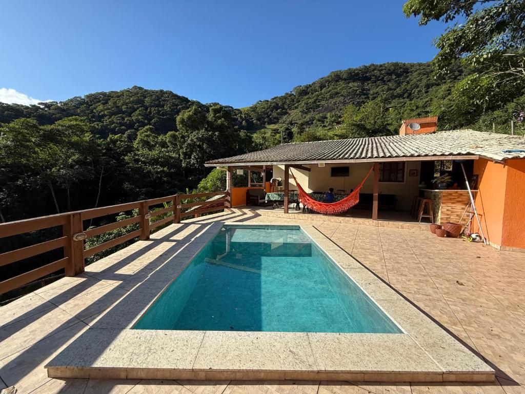a swimming pool next to a house with a hammock at Sana - Chácara Canto do Tiê - 15 hospedes in Casimiro de Abreu