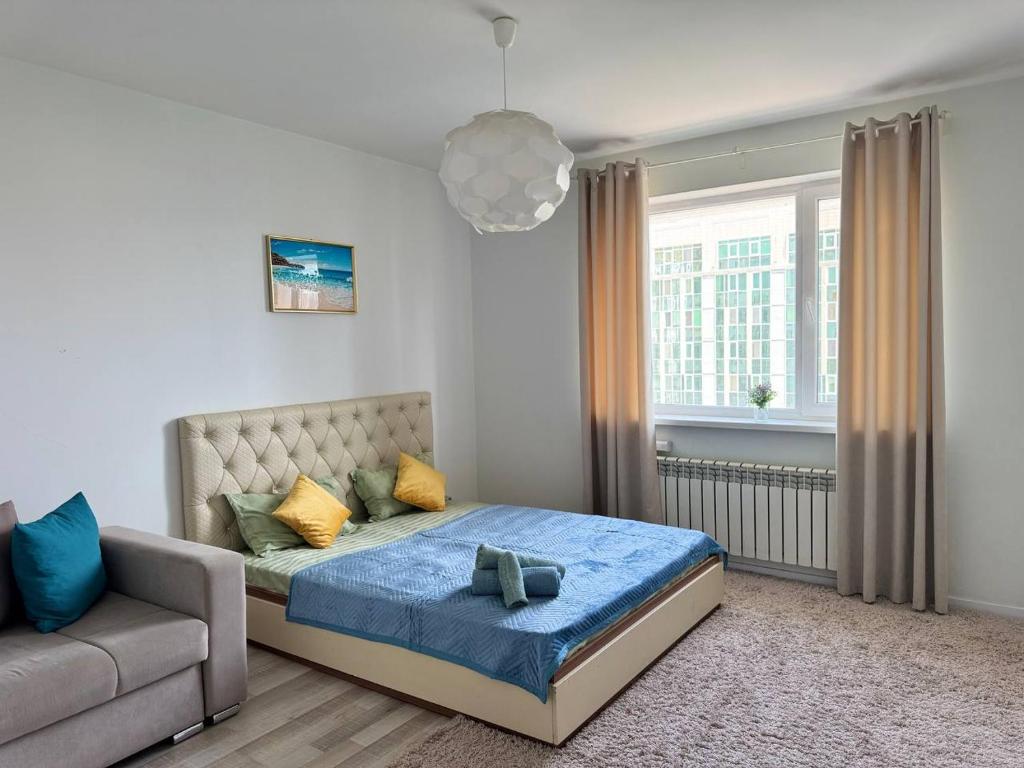 a bedroom with a bed and a couch and a window at ЖК Времена года Весна Кабанбай Батыра 46 in Taldykolʼ