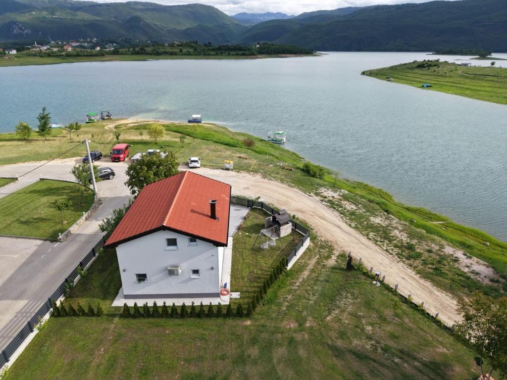 a white house with a red roof next to a lake at Vikendica Bošnjak in Prozor