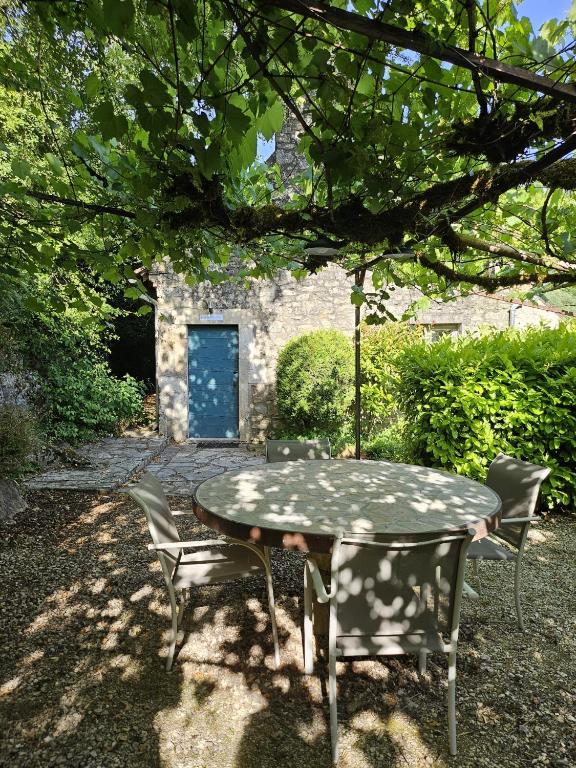 une table et des chaises sous un arbre avec une porte bleue dans l'établissement Les Pieds dans l'eau, Gîte Le Blagour, à Lachapelle-Auzac