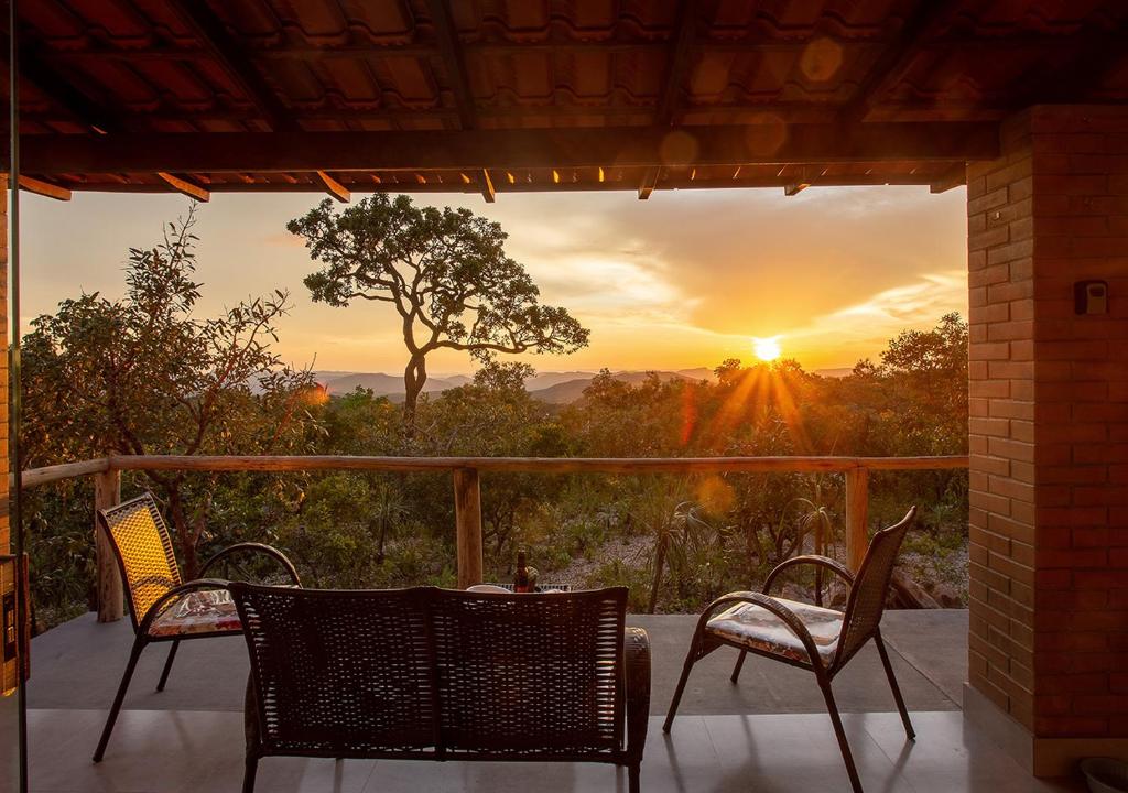 a patio with chairs and a table and a sunset at Chalé Belvedere Veadeiros in Alto Paraíso de Goiás