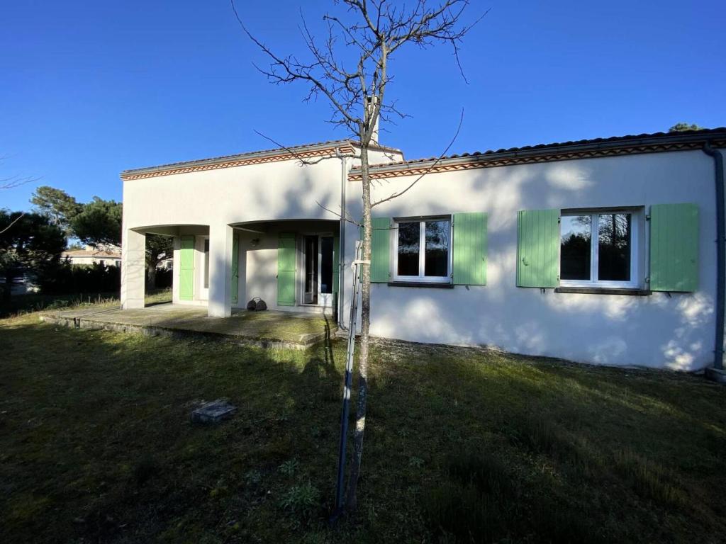 une maison blanche avec un arbre dans la cour dans l'établissement Résidence 121-montalivet - 121 - Agréable maison de vacances dans Montalivet MAE-4891, à Vendays-Montalivet