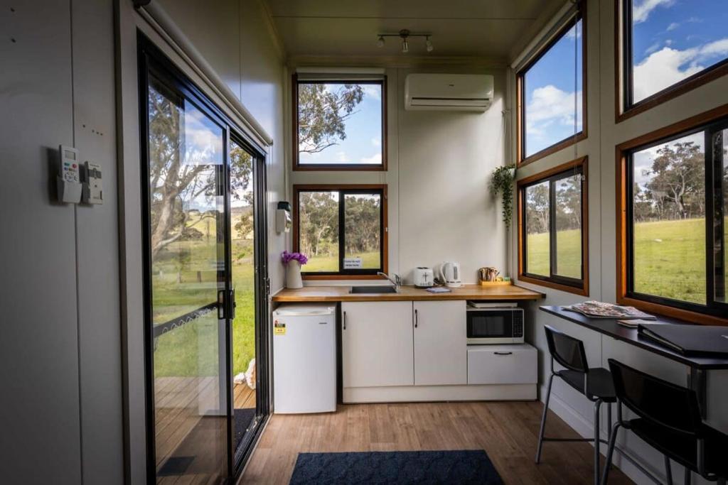 una cucina con armadietti bianchi, finestre e bancone di Sithuri Tiny House by Tiny Away a Windeyer