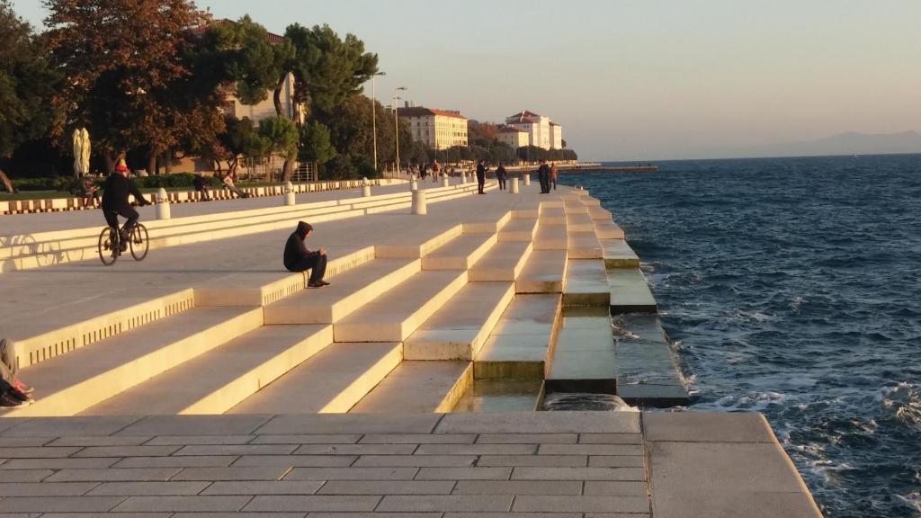 a person sitting on a bench next to the water at Green lighthouse rooms in Zadar