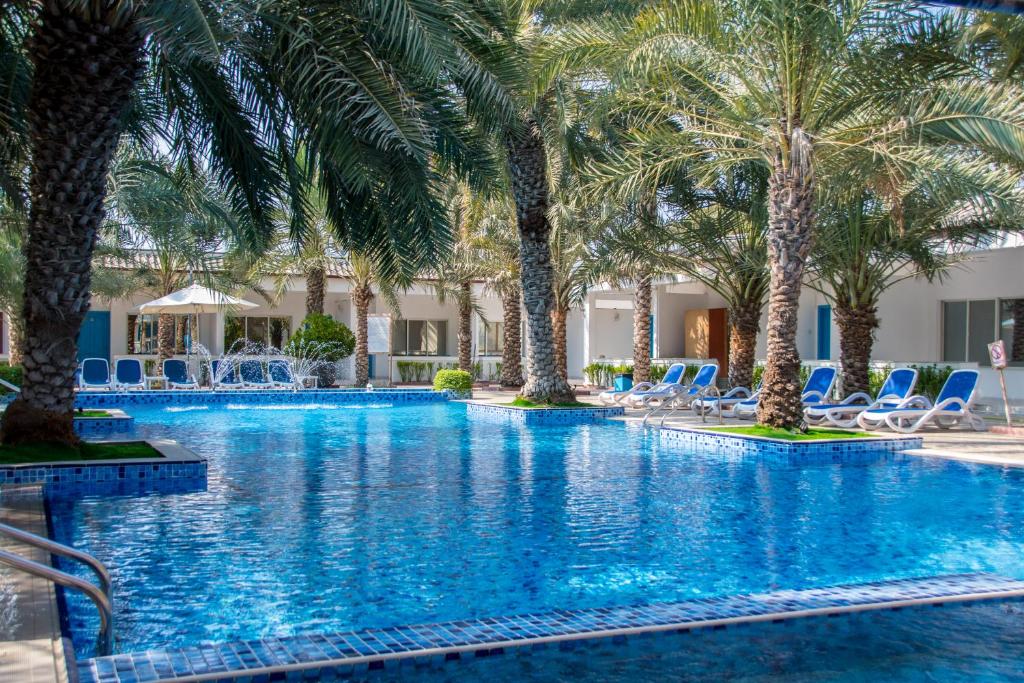 a pool with palm trees and lounge chairs at Fujairah Hotel & Resort in Fujairah
