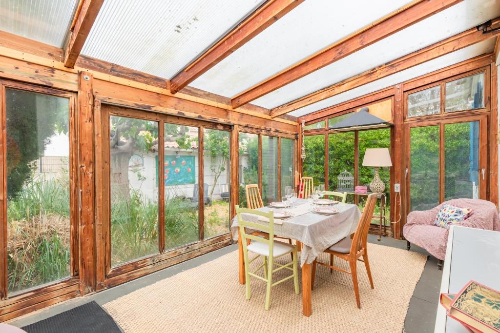 une véranda avec une table, des chaises et des fenêtres dans l'établissement Le Chalet des Eucalyptus - à 200 m de la plage, à Fleury
