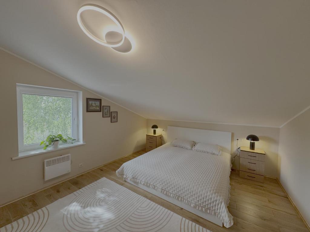 a white bedroom with a bed and a window at Po Beržu in Molėtai