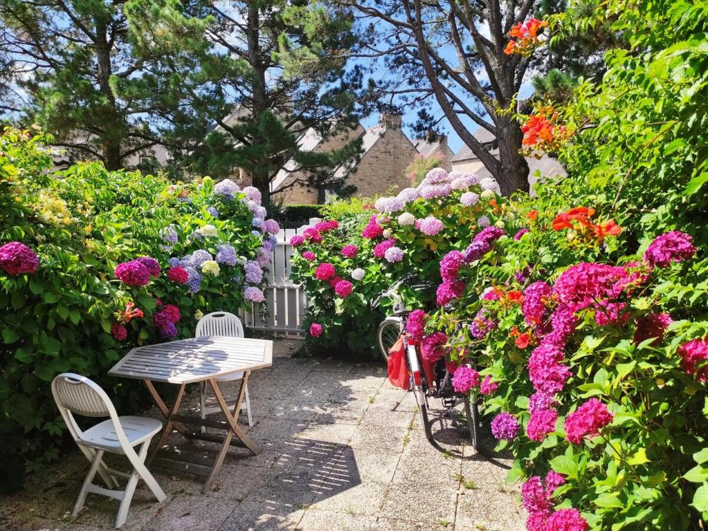 un jardin avec une table, des chaises et des fleurs dans l'établissement Les Galiotes - Maison à Carnac proche plage, à Carnac