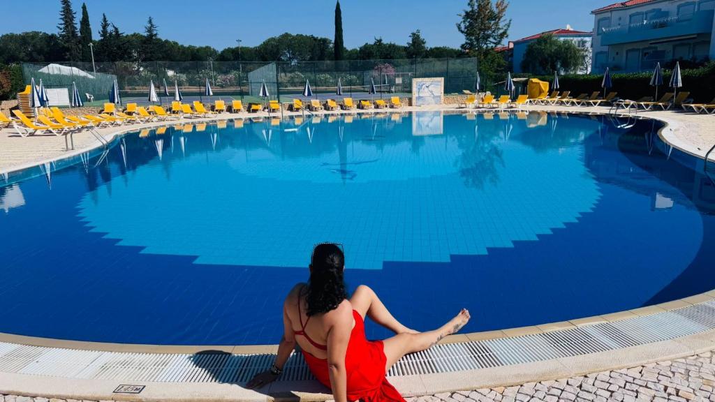 a woman sitting next to a large swimming pool at Villa Oasis Parque BY SWEET HOME in Portimão