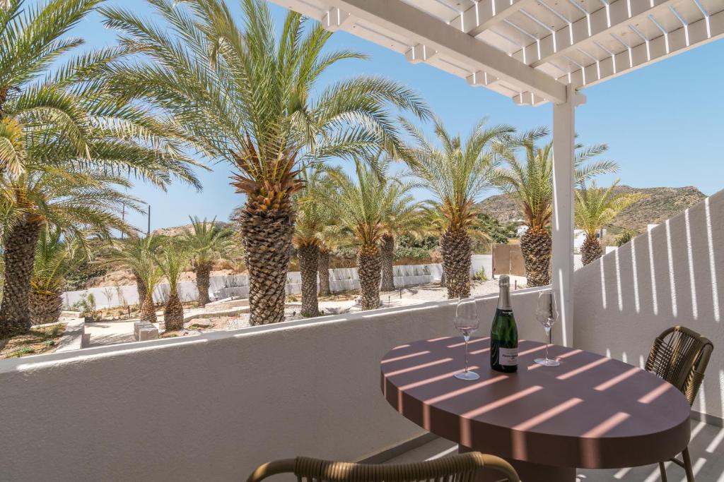 a table with a bottle of wine on a balcony with palm trees at Golden Milos Beach Ηouse by Domotel in Provatas