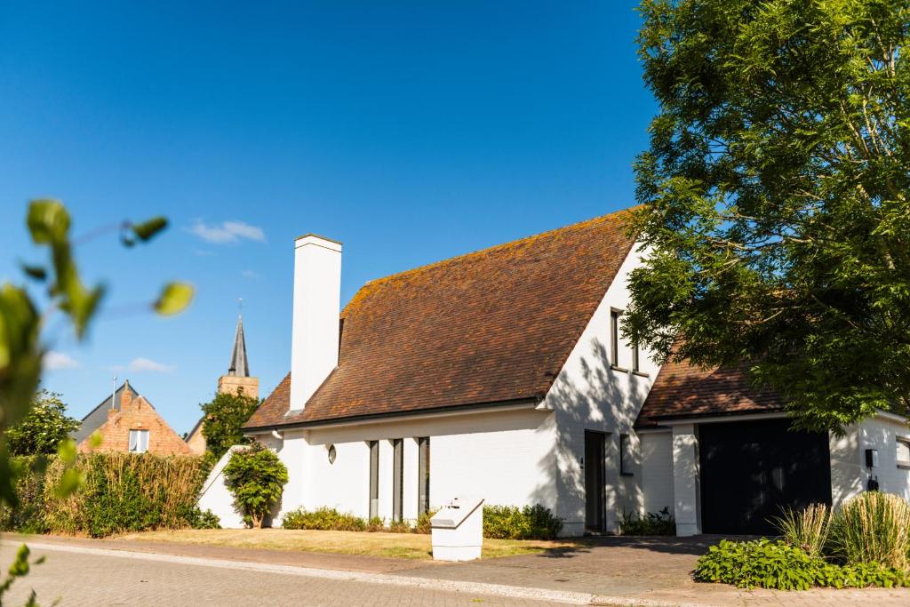 ein weißes Haus mit einem braunen Dach und einer Kirche in der Unterkunft Villa Croisette in Nieuwpoort