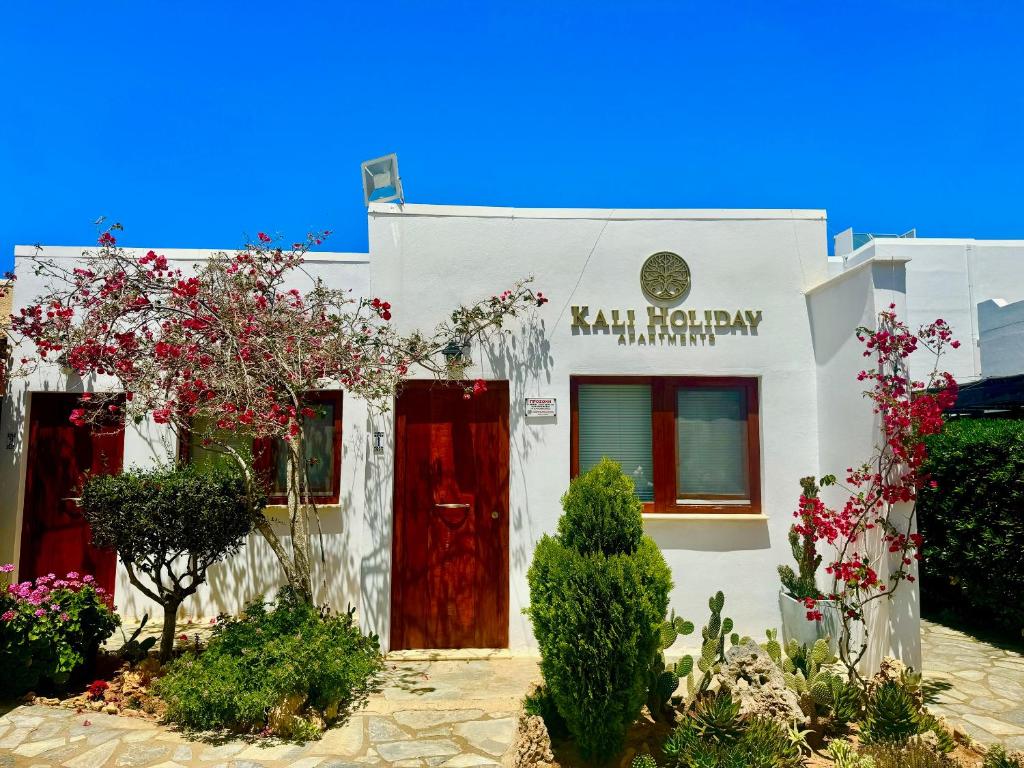 a white building with red doors and flowers at Kali Holiday Apartments in Stalida