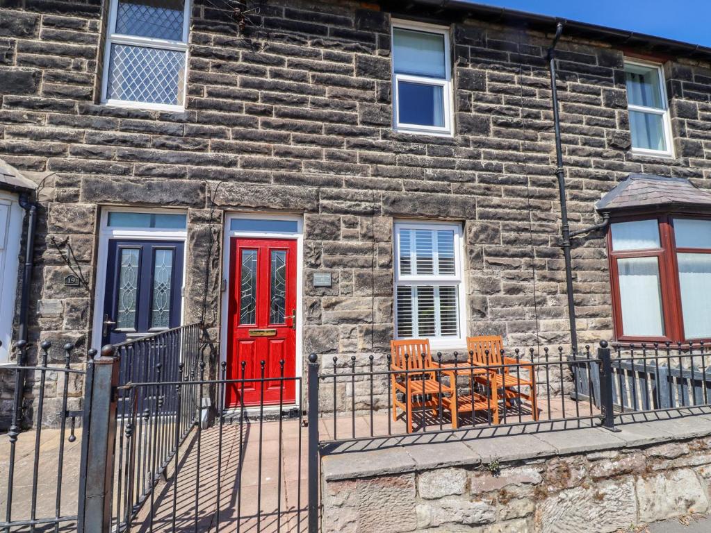 a stone building with red doors and chairs in front of it at Kennie Cottage in Seahouses