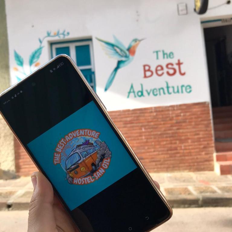 a person holding a cell phone with the best adventure logo on it at The Best Adventure Hostel in San Gil