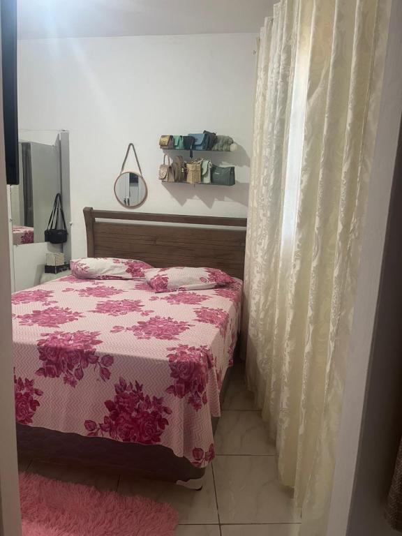 a bedroom with a bed with a pink blanket and a curtain at Kitnet Luar in São Thomé das Letras