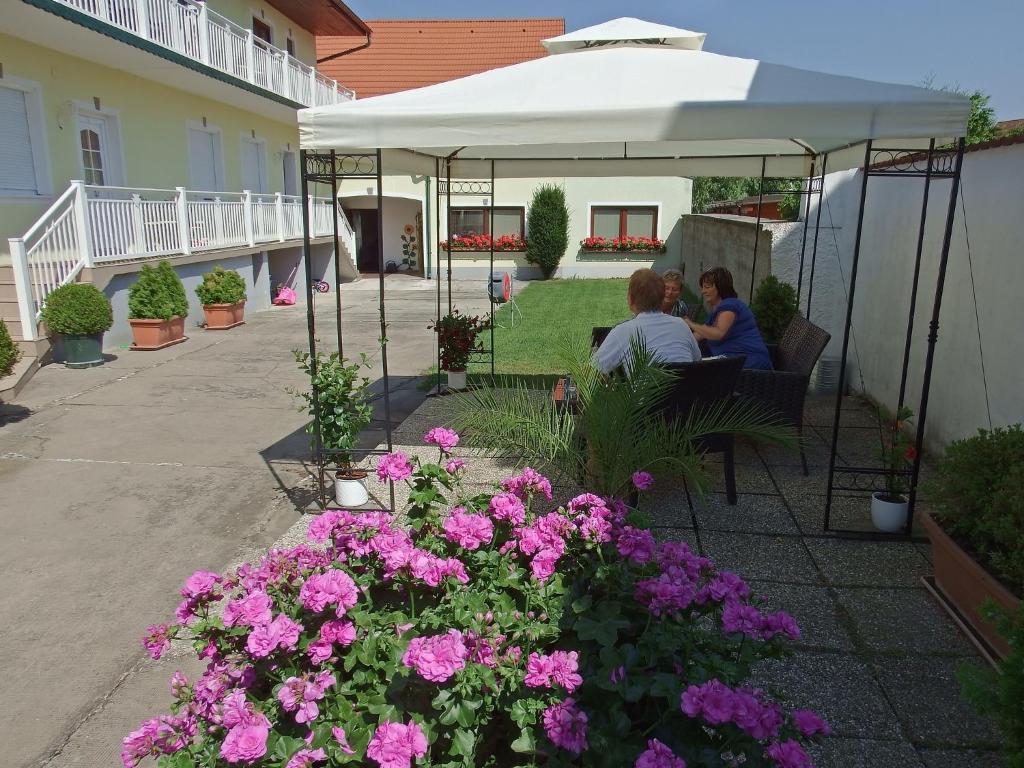 dos personas sentadas bajo un paraguas en un patio con flores rosas en Gästehaus - Doris - Wenzl, en Mörbisch am See