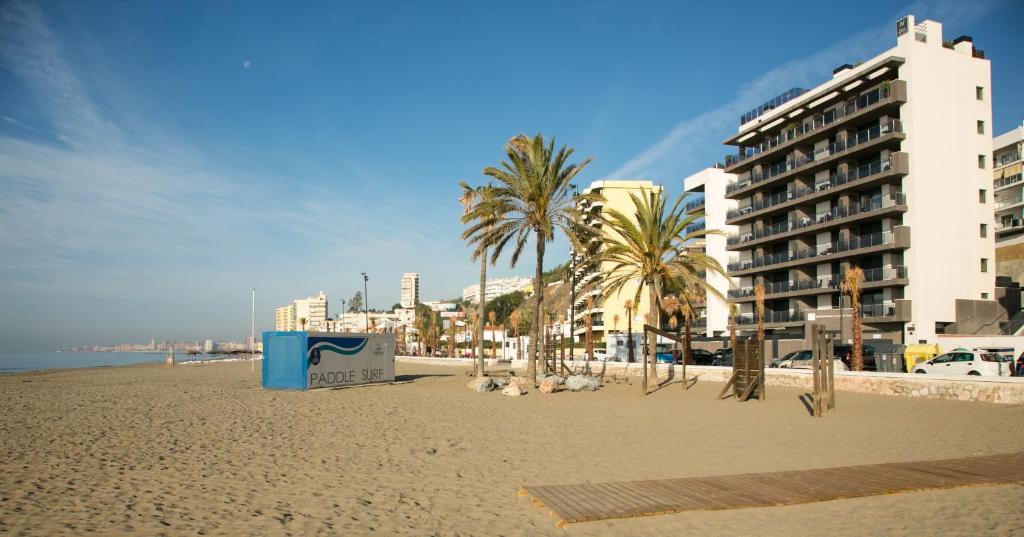 una playa de arena con palmeras y un edificio en Apartamentos Fuengirola Playa en Fuengirola