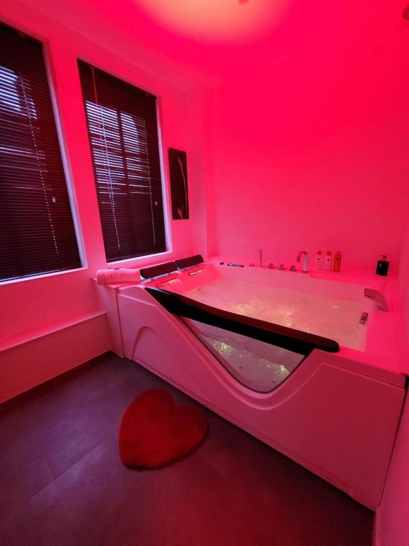 une salle de bain rose avec une baignoire avec une lumière rouge dans l'établissement Loveroom Instants Secret Amiens, à Amiens