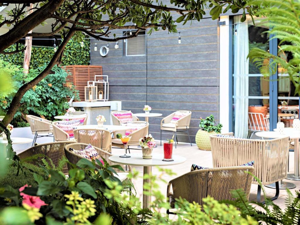 an outdoor patio with tables and chairs and plants at Croisette Beach Hotel Cannes - MGallery Collection in Cannes