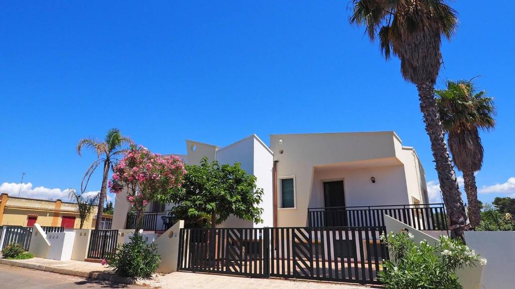 a white house with a fence and palm trees at Appartamenti Torre Suda by Salento Affitti in Torre Suda