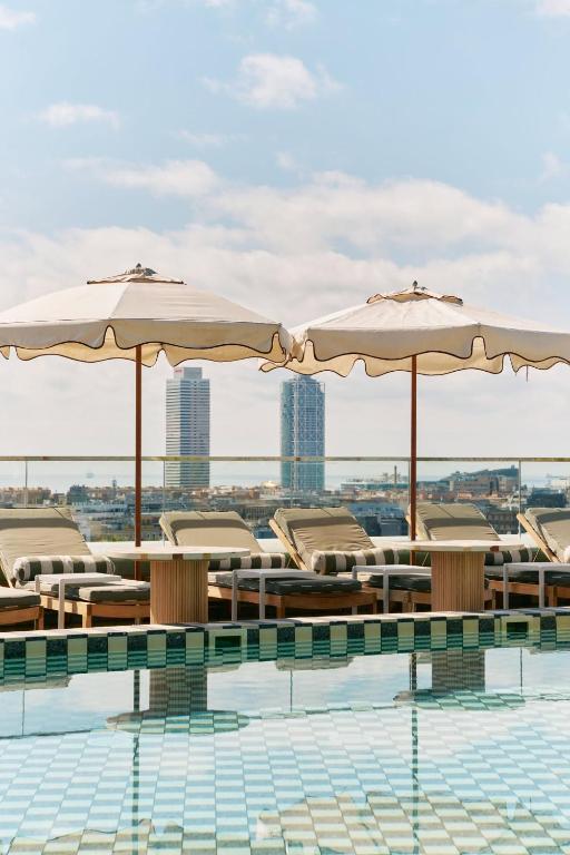 a pool with lounge chairs and umbrellas at The Hoxton, Poblenou in Barcelona