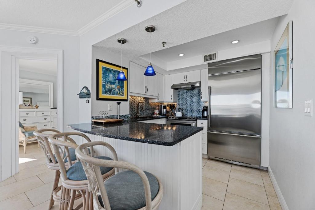a kitchen with a counter with chairs and a refrigerator at Palm House 3B with oceanfront views, pool, and private beach access in New Smyrna Beach