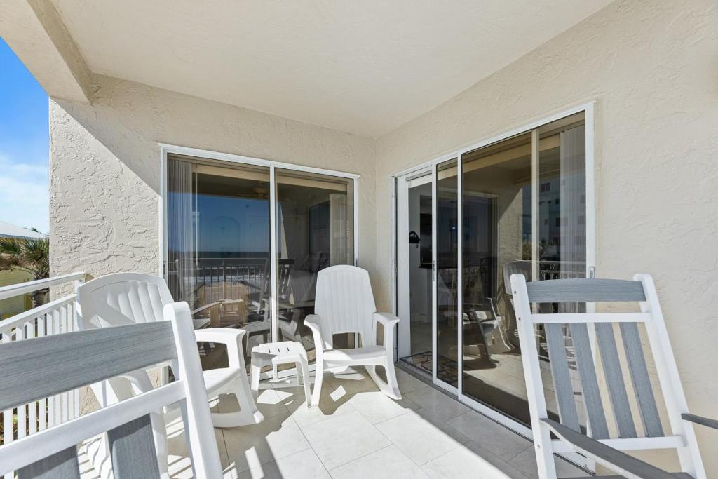 a porch with white chairs and a table on a balcony at Palm House 3B with oceanfront views, pool, and private beach access in New Smyrna Beach