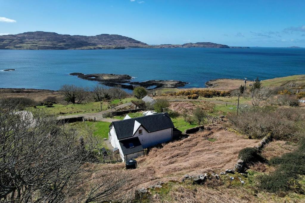 a house on a hill next to a body of water at Grouse Cottage in Kilninian