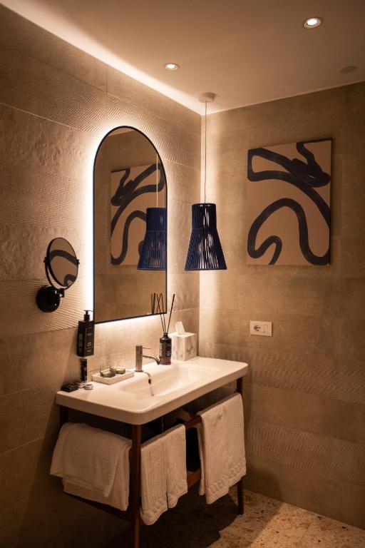 a bathroom with a sink and a mirror and towels at Cala Ponte, a Tribute Portfolio Hotel in Polignano a Mare