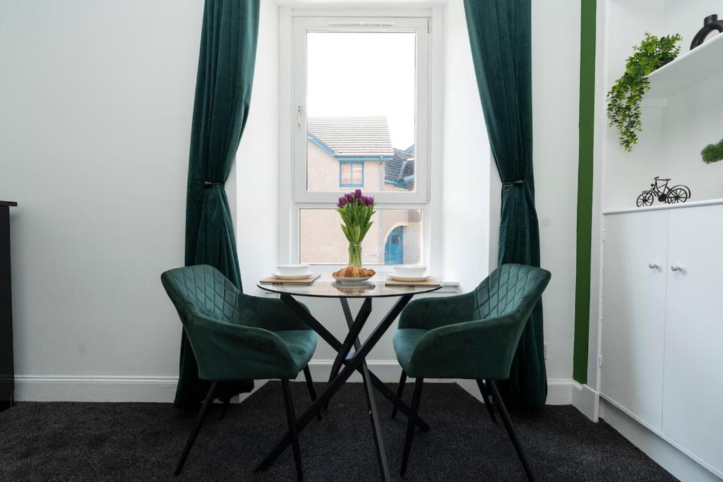 a table with two green chairs and a window at Studio flat in Dundee in Dundee
