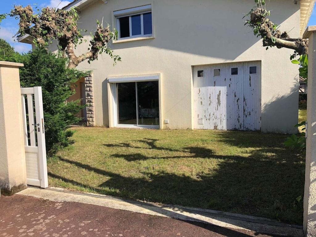 une maison avec une porte blanche et une cour en gazon dans l'établissement Maison 2 chambres et 2 lits simple Jardin en centre ville, à Carcans