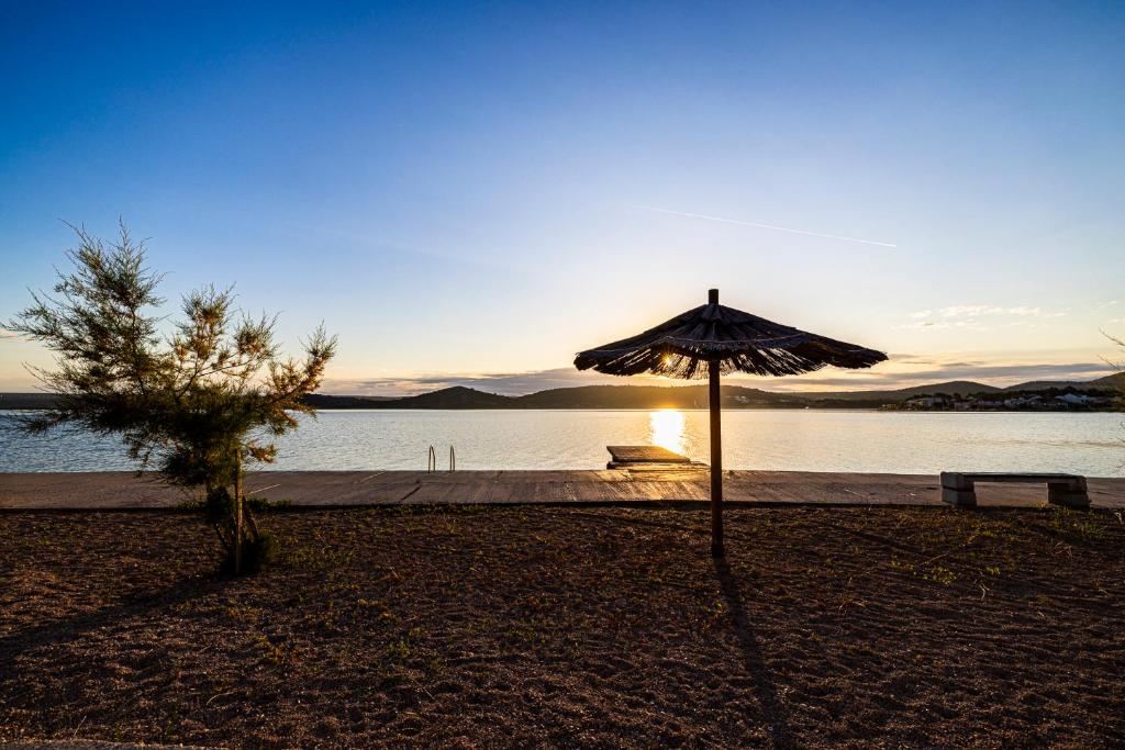 an umbrella sitting on the beach with the sun setting at Sydney Apartment in Bilice