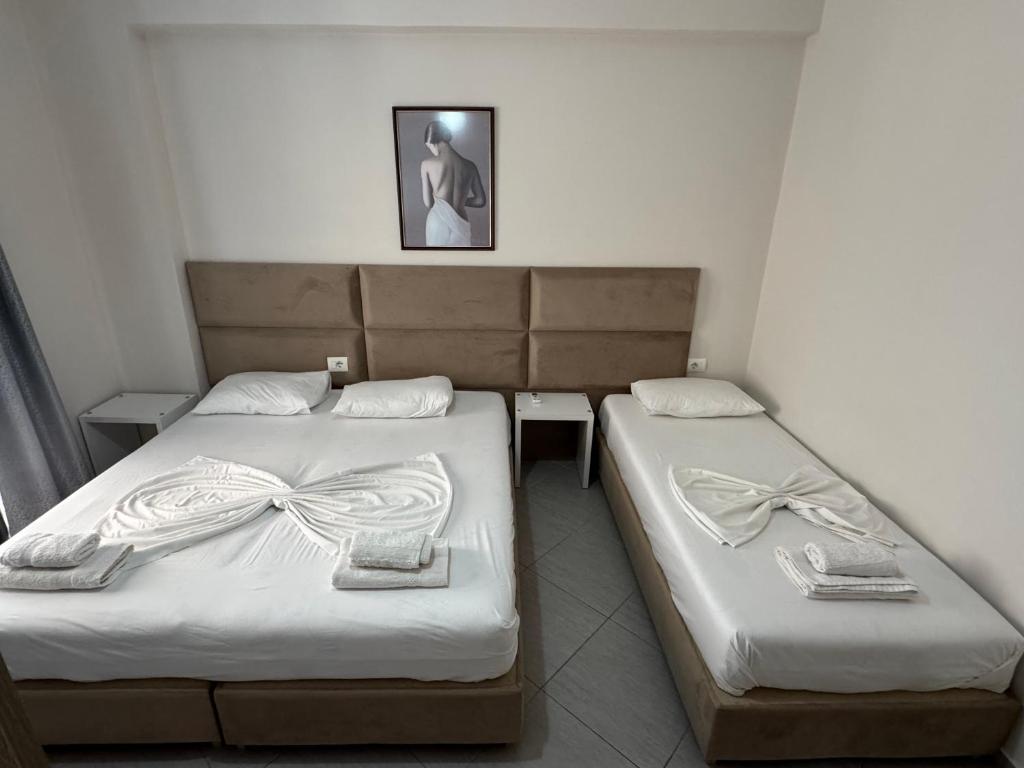 two beds in a hotel room with white sheets at Gersa's Family Studios in Sarandë