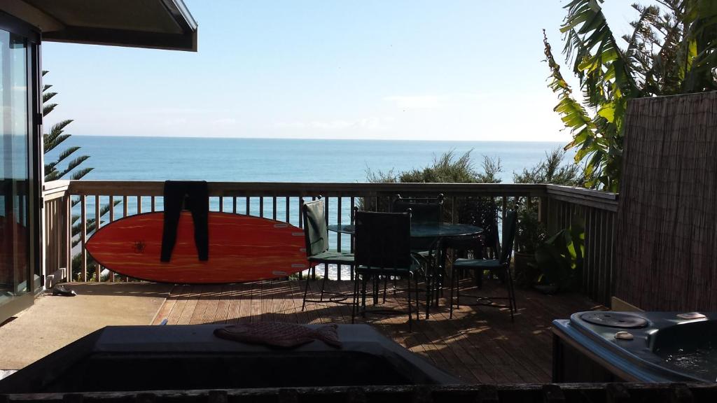 a red surfboard sitting on a deck with the ocean at G SPOT UPPER LEVEL with spa in Raglan