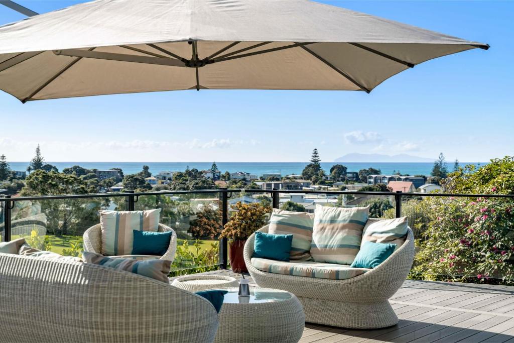 un patio avec deux chaises et un parasol dans l'établissement Island Views - Waihi Beach Holiday Home, à Waihi Beach