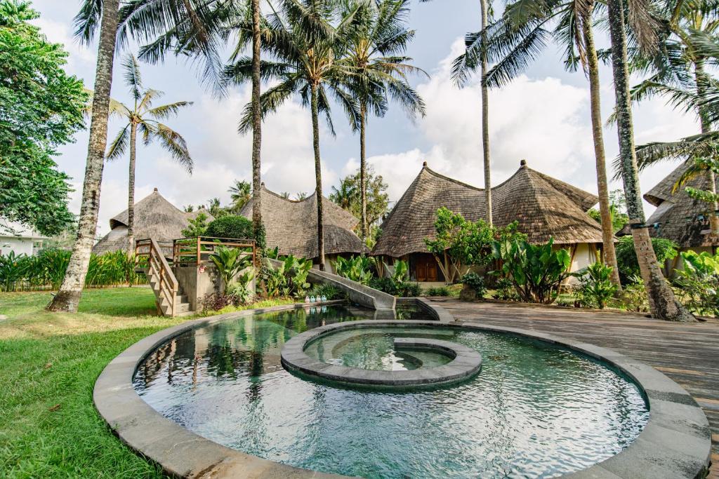 a pool in front of a resort with palm trees at Hemma Human Home in Ubud