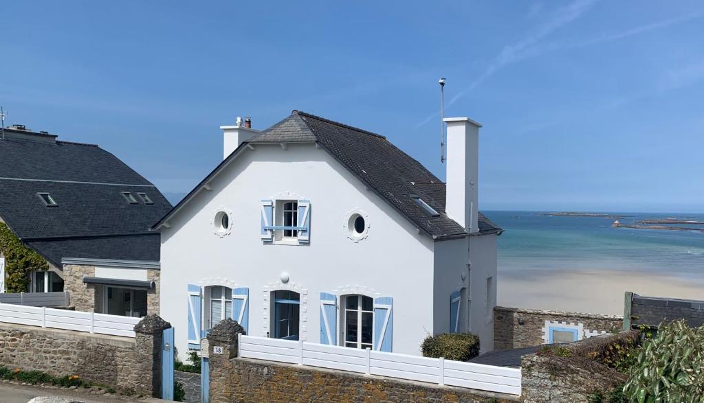 une maison blanche avec un toit noir et l'océan dans l'établissement TY KERVIGORN les pieds dans l'eau, à Saint-Pabu