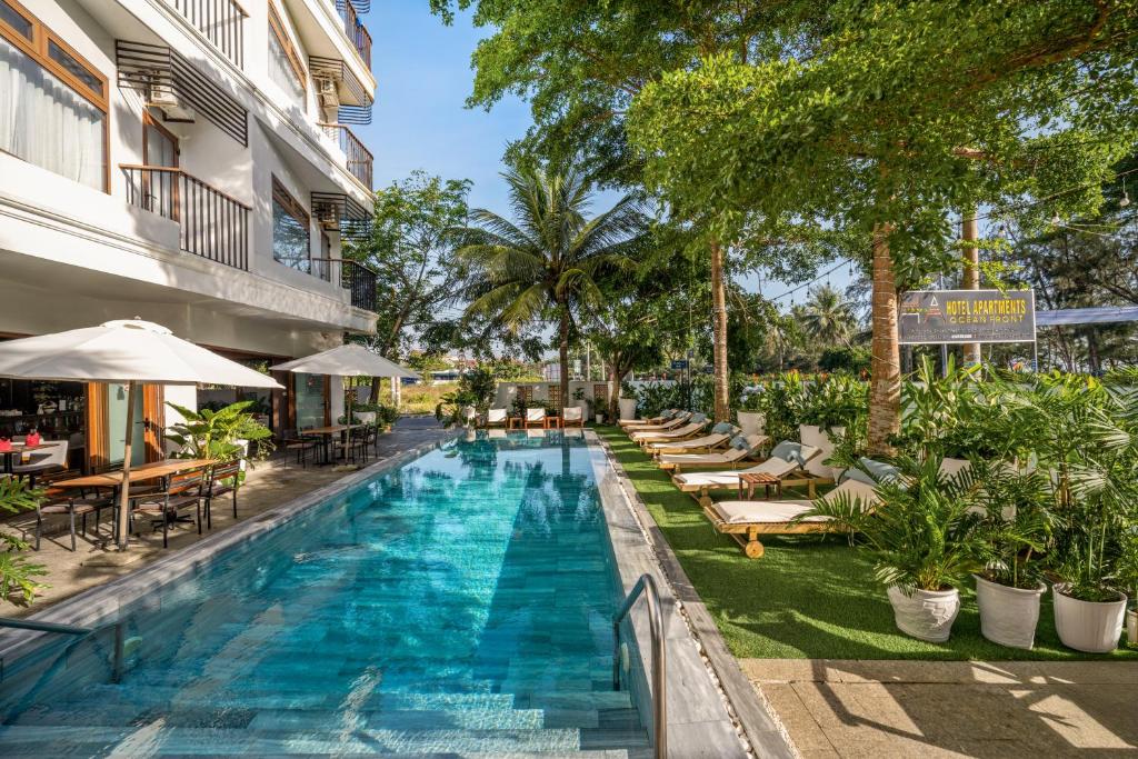 a swimming pool with lounge chairs and tables next to a building at HA Ocean Front Hotel and Apartment in Hoi An