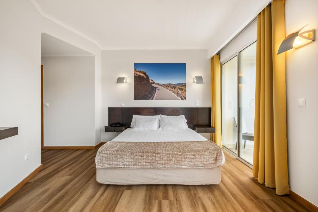 a bedroom with a large bed and wooden floors at White Waters Hotel in Machico