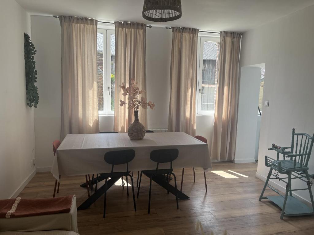 Una mesa de comedor con sillas y un jarrón encima. en Ferme Cosy et Paisible au Bord de l'Eure, en Criquebeuf-sur-Seine