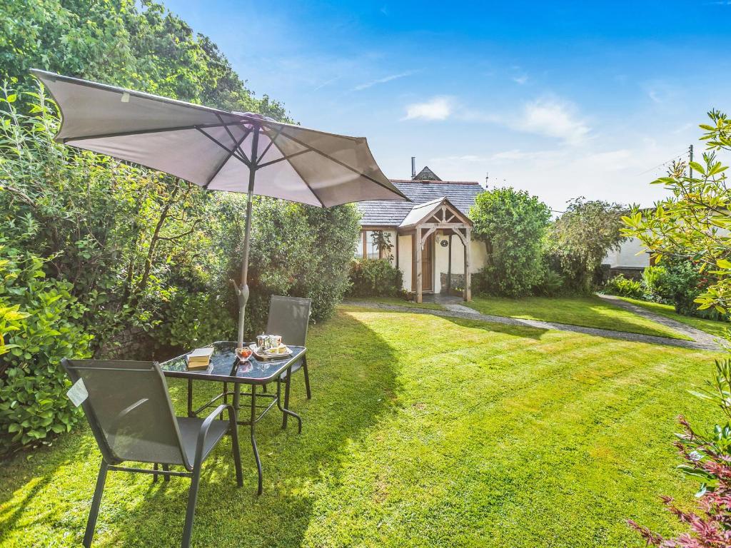 einen Tisch und Stühle mit Sonnenschirm im Hof in der Unterkunft Rose Cottage in Hartland