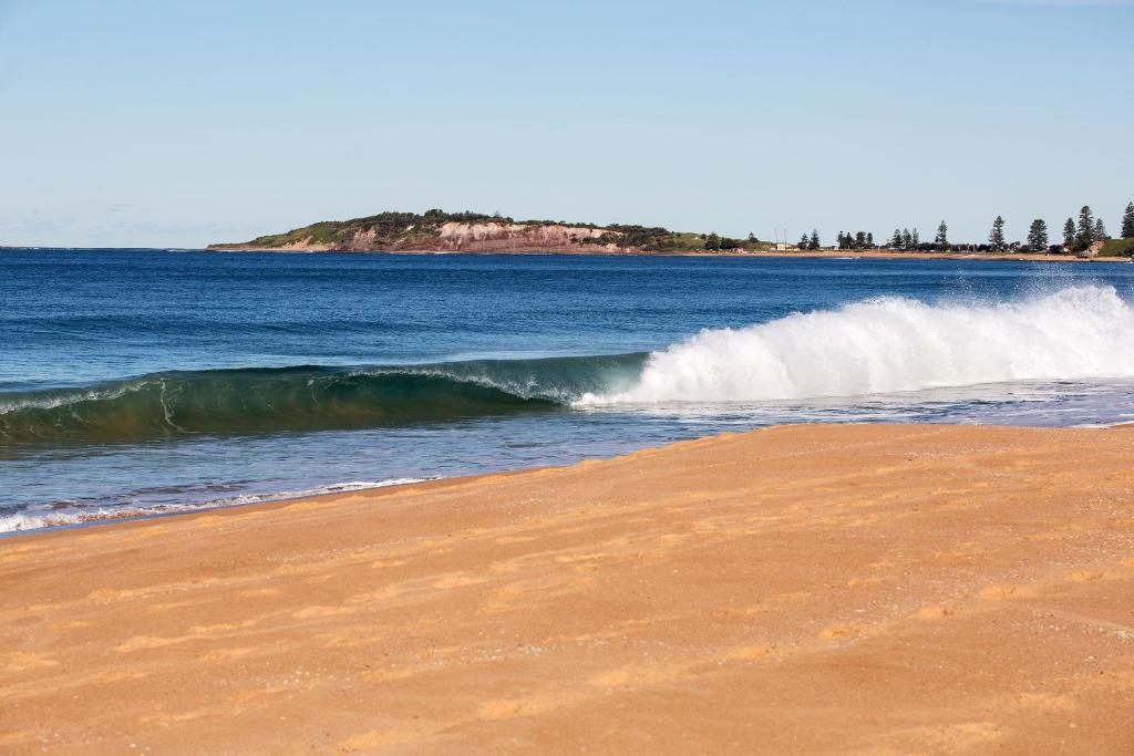a wave in the ocean next to a sandy beach at Narrabeen Sands Hotel by Nightcap Plus in Narrabeen