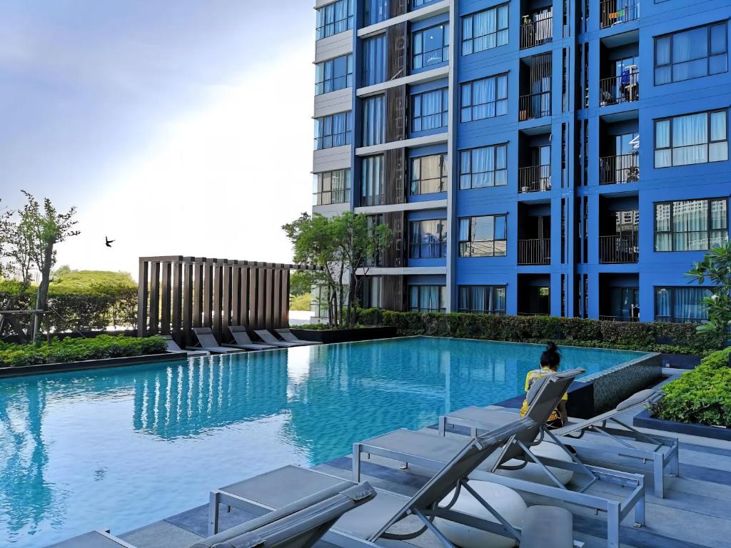 a woman sitting in a chair next to a swimming pool at The Base - Rama 9 by Sumaq Property in Bangkok